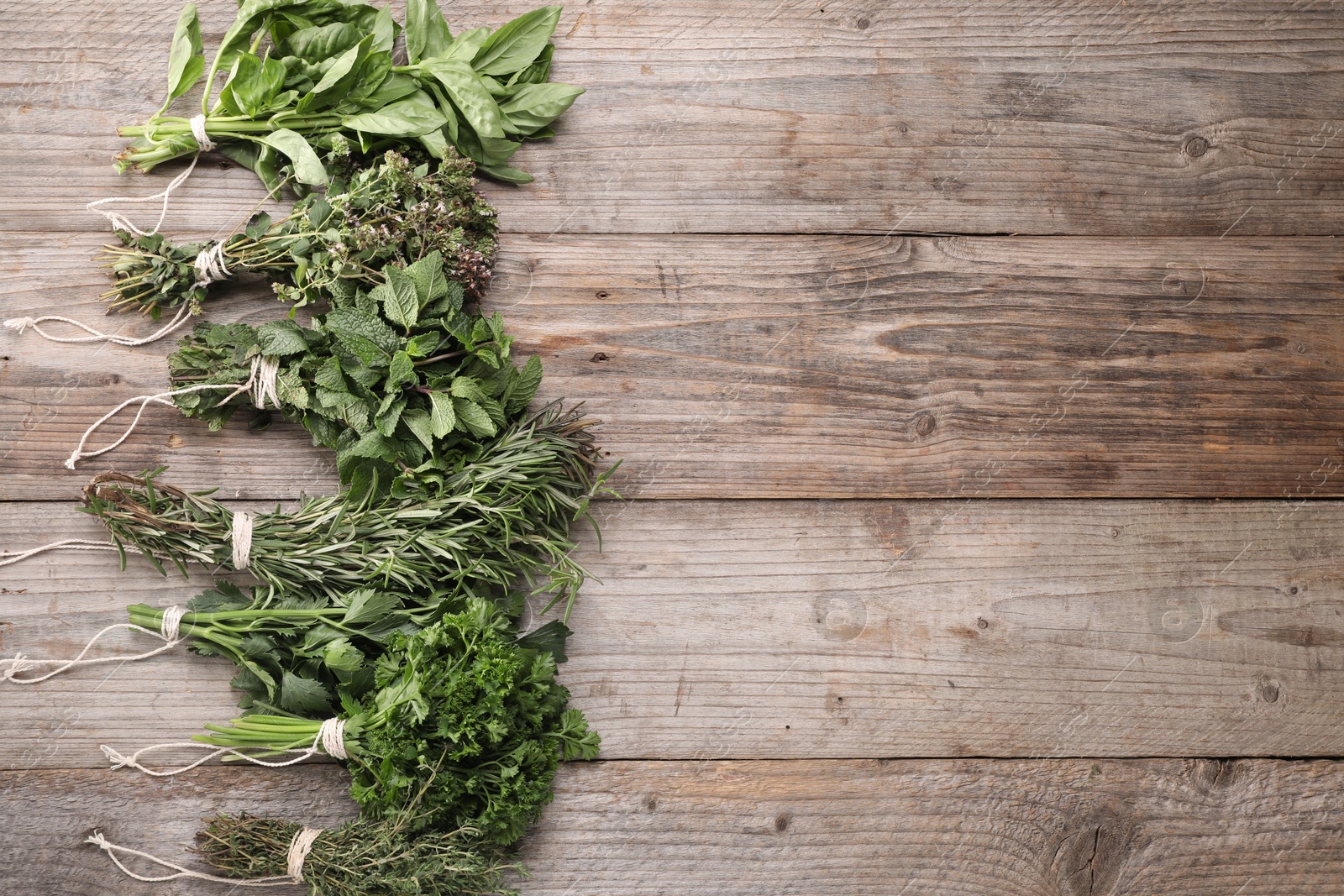 Photo of Bunches of different aromatic herbs on wooden table, flat lay. Space for text