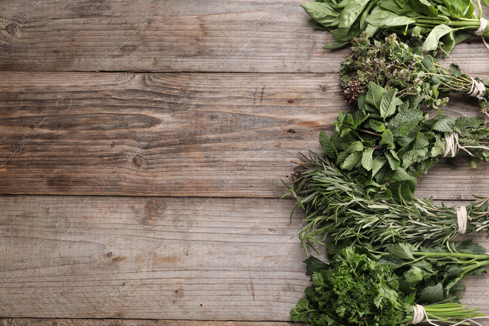 Photo of Bunches of different aromatic herbs on wooden table, flat lay. Space for text