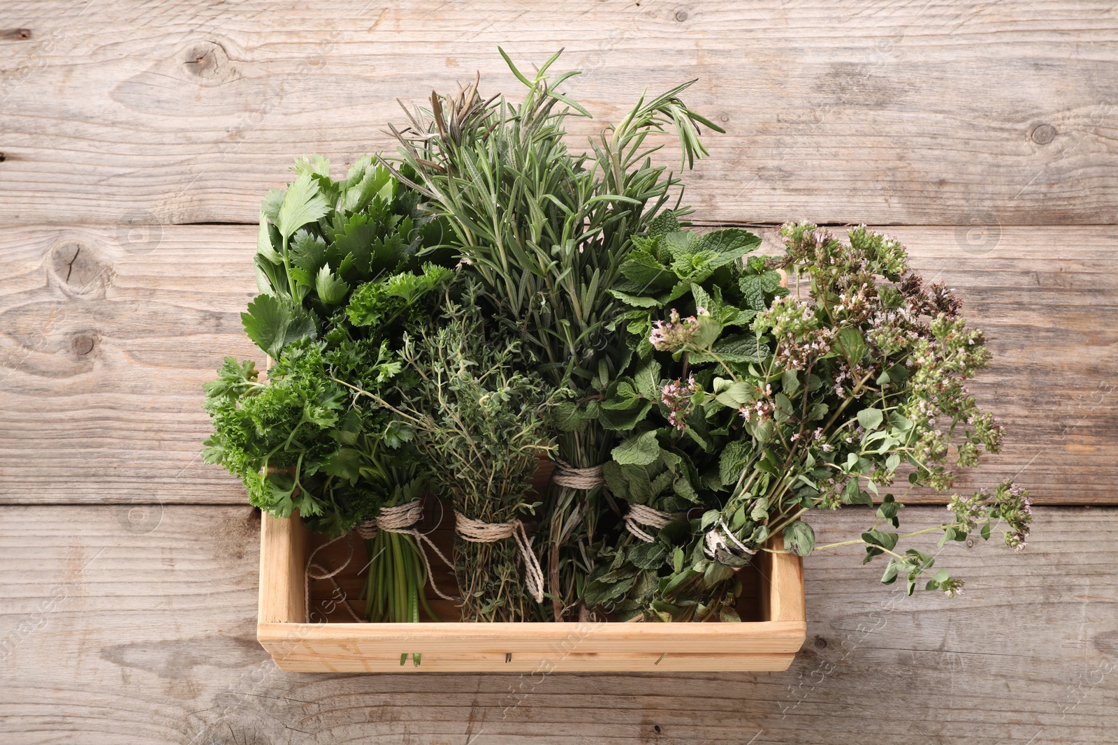 Photo of Bunches of different aromatic herbs in crate on wooden table, above view