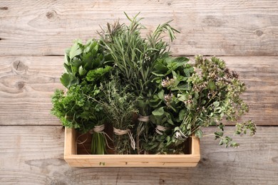 Photo of Bunches of different aromatic herbs in crate on wooden table, above view