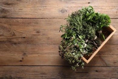 Photo of Bunches of different aromatic herbs in crate on wooden table, top view. Space for text