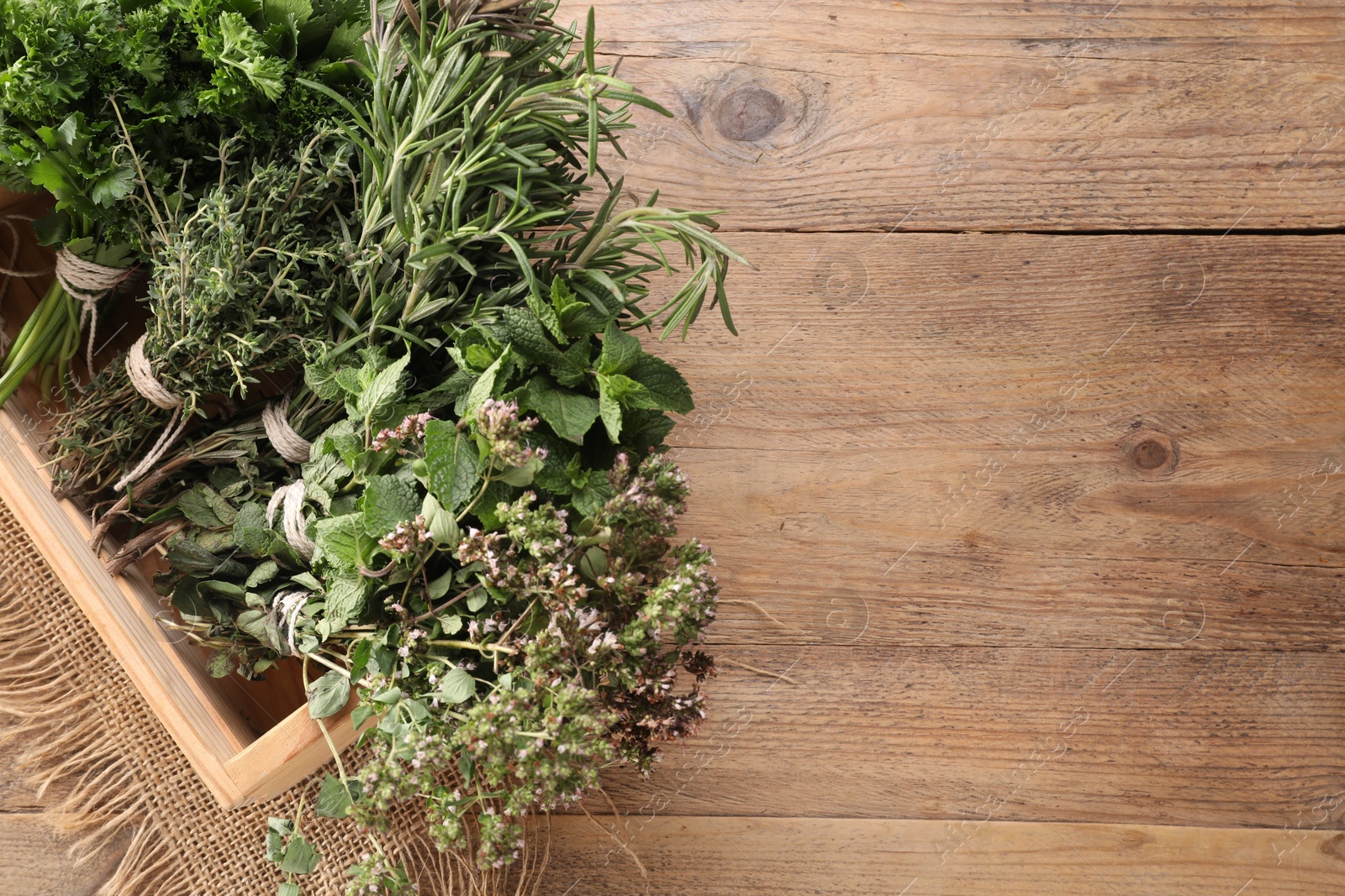 Photo of Bunches of different aromatic herbs in crate on wooden table, above view. Space for text