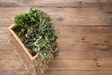 Photo of Bunches of different aromatic herbs in crate on wooden table, top view. Space for text