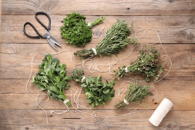 Bunches of different aromatic herbs, spool of thread and scissors on wooden table, flat lay