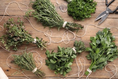 Photo of Bunches of different aromatic herbs, rope and scissors on wooden table, flat lay