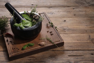 Photo of Mortar with different aromatic herbs on wooden table, space for text