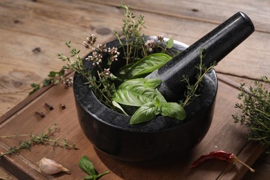 Photo of Mortar with different aromatic herbs on wooden table, closeup