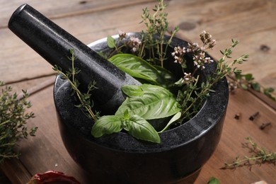 Photo of Mortar with different aromatic herbs on wooden table, closeup