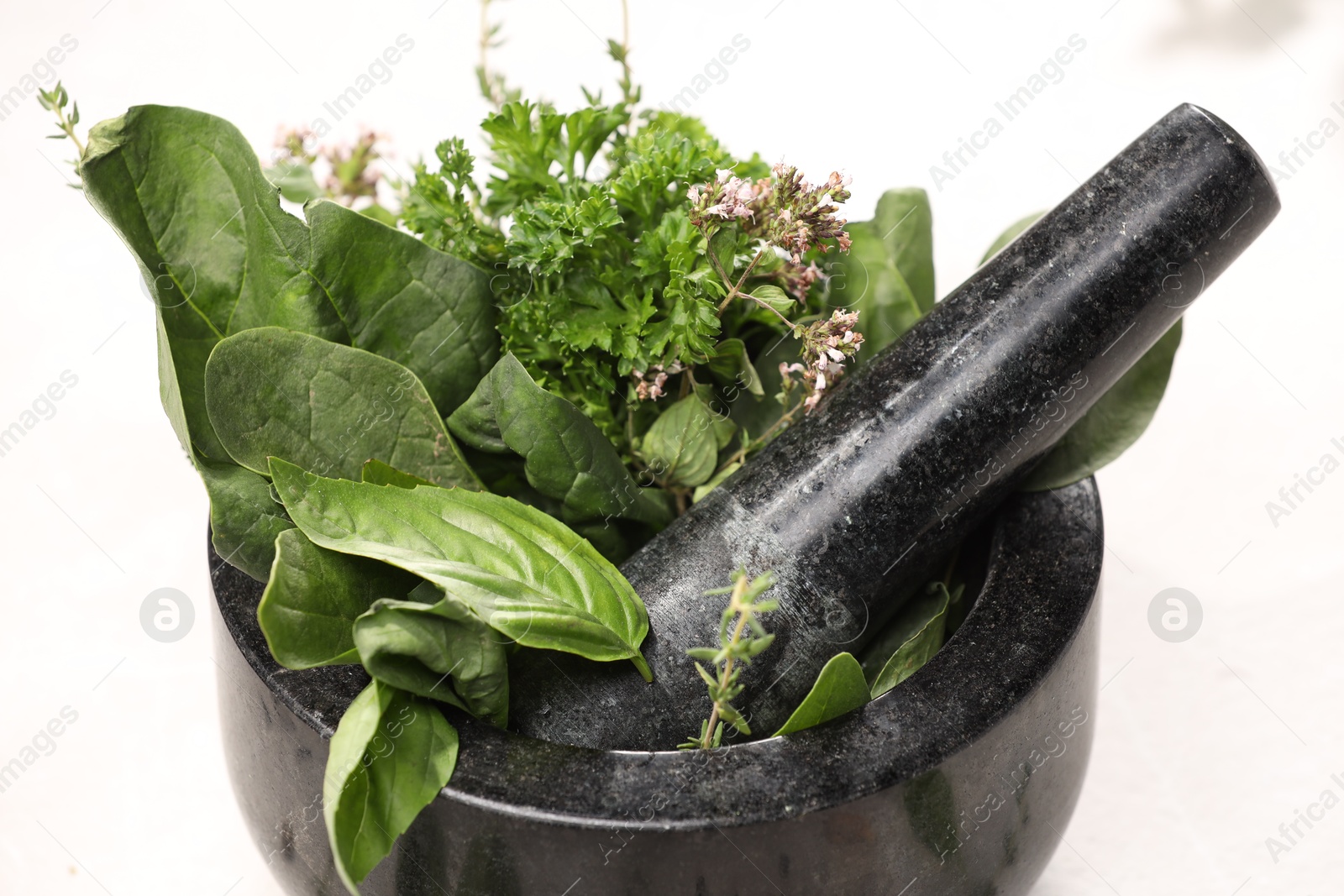 Photo of Different aromatic herbs in mortar on white table, closeup