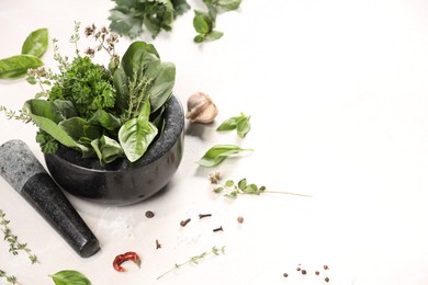 Photo of Mortar with different aromatic herbs on white table, space for text