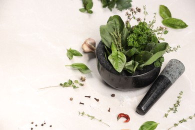 Mortar with different aromatic herbs on white table, space for text