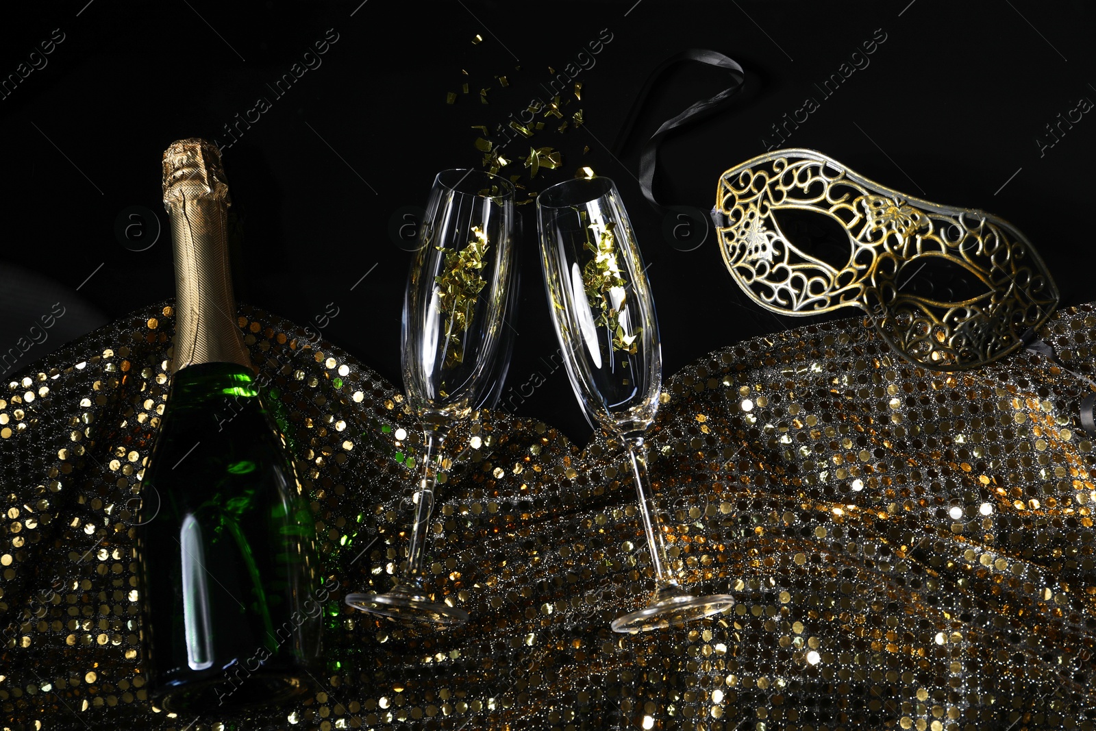 Photo of Beautiful carnival masks, champagne, glasses and fabric with golden sequins on black background, flat lay