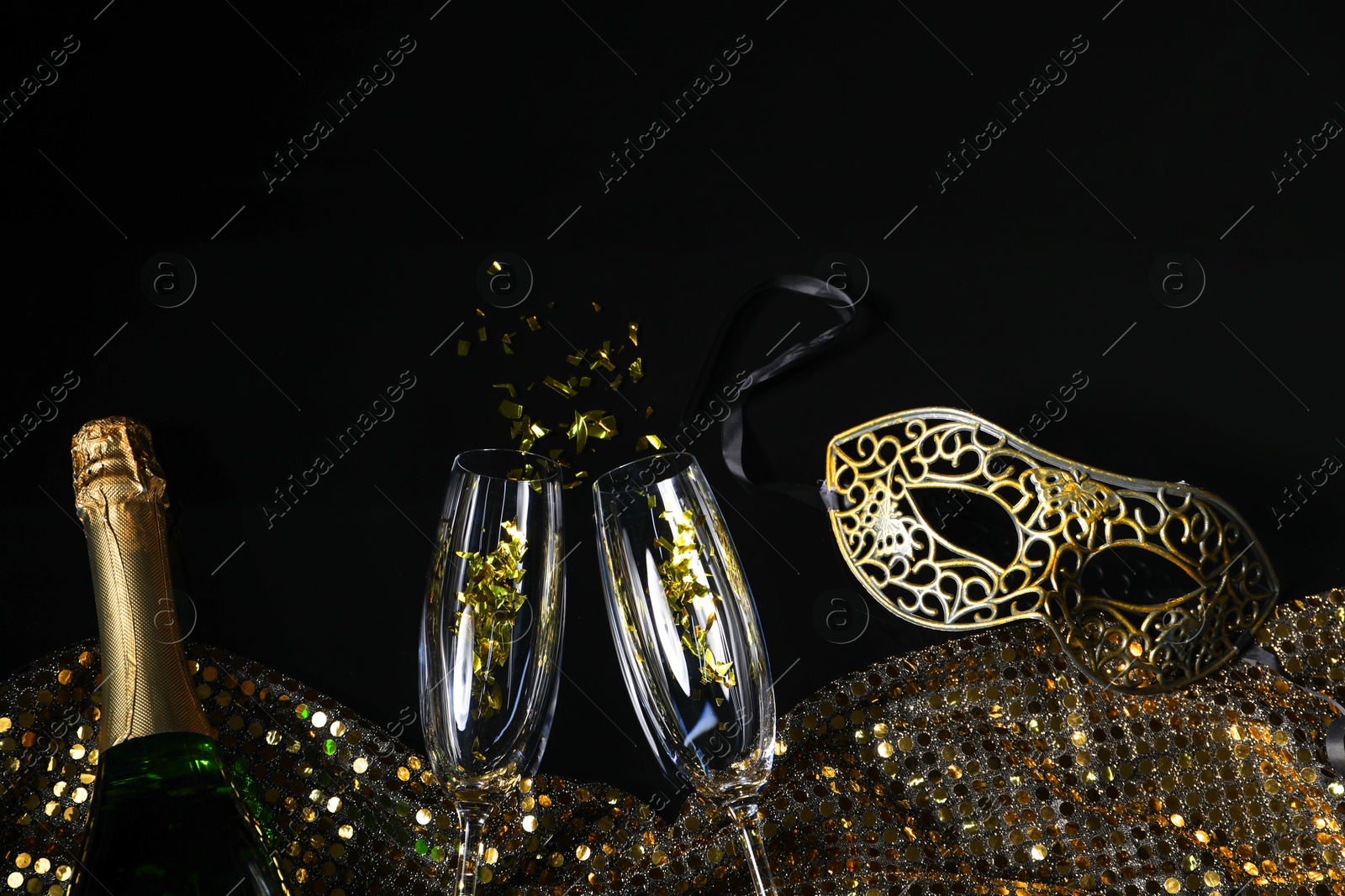 Photo of Beautiful carnival masks, champagne, glasses and fabric with golden sequins on black background, flat lay