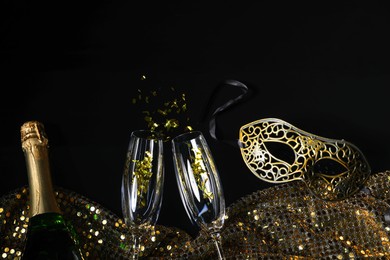 Beautiful carnival masks, champagne, glasses and fabric with golden sequins on black background, flat lay