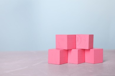 Photo of Blank pink cubes on light grey marble table, space for text