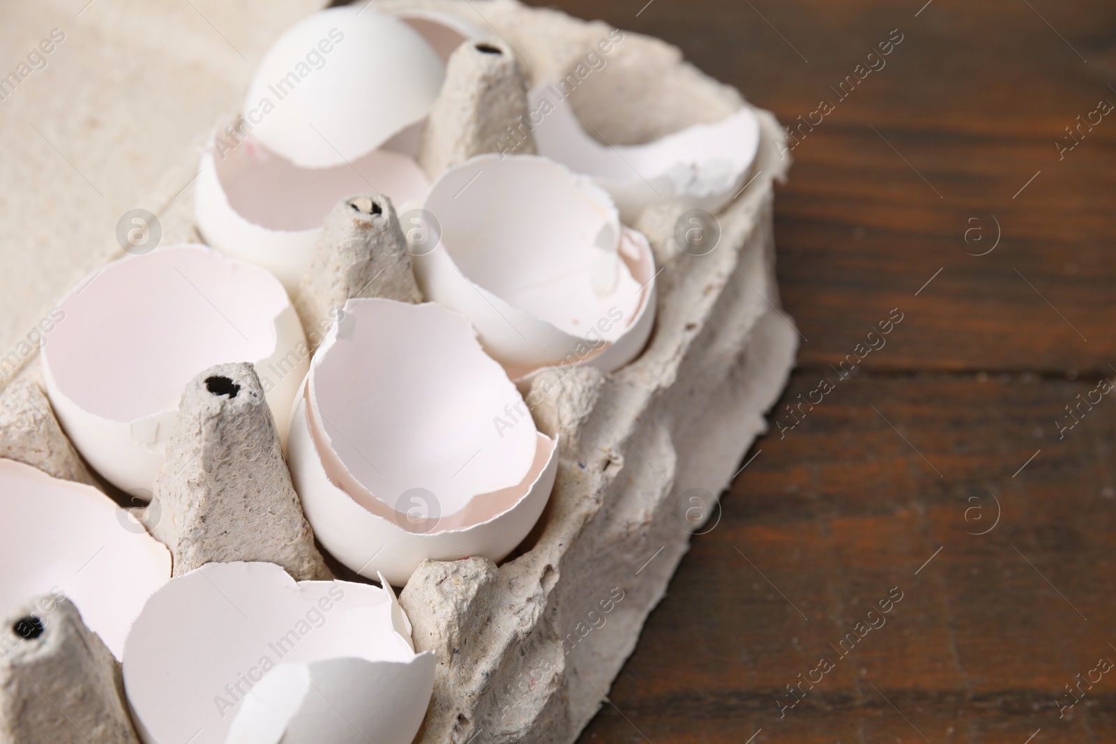 Photo of Broken eggshells in carton on wooden table, closeup. Space for text