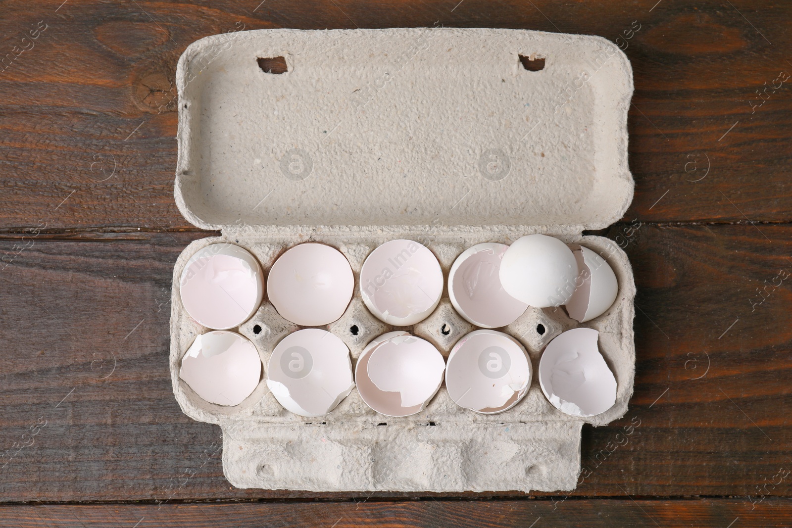 Photo of Broken eggshells in carton on wooden table, top view