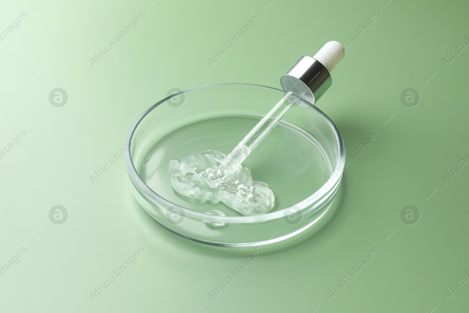 Photo of Petri dish with cosmetic product and pipette on green background