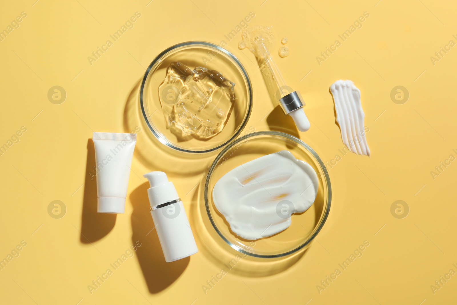 Photo of Petri dishes with cosmetic products and pipette on yellow background, flat lay