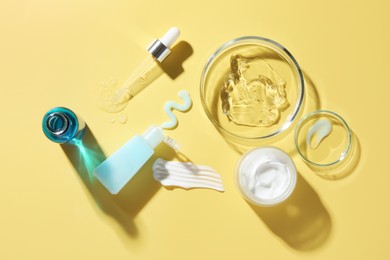 Photo of Petri dishes with cosmetic products and pipette on yellow background, flat lay