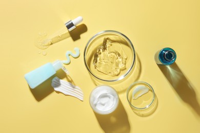 Photo of Petri dishes with cosmetic products and pipette on yellow background, flat lay