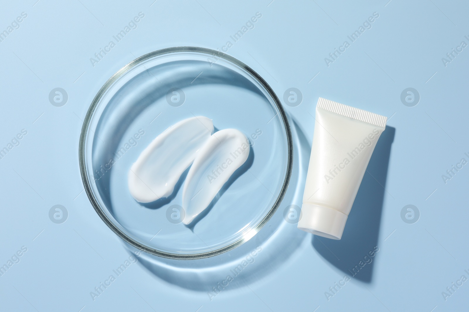 Photo of Petri dish with cosmetic product and tube on light blue background, flat lay