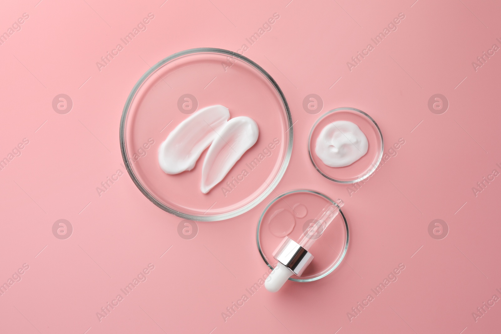 Photo of Petri dishes with cosmetic products and pipette on pink background, flat lay