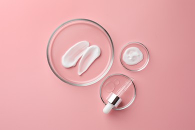 Photo of Petri dishes with cosmetic products and pipette on pink background, flat lay