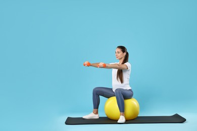 Photo of Beautiful pregnant woman with dumbbells doing exercises on fitball against light blue background