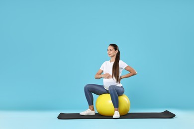 Photo of Beautiful pregnant woman doing exercises on fitball against light blue background