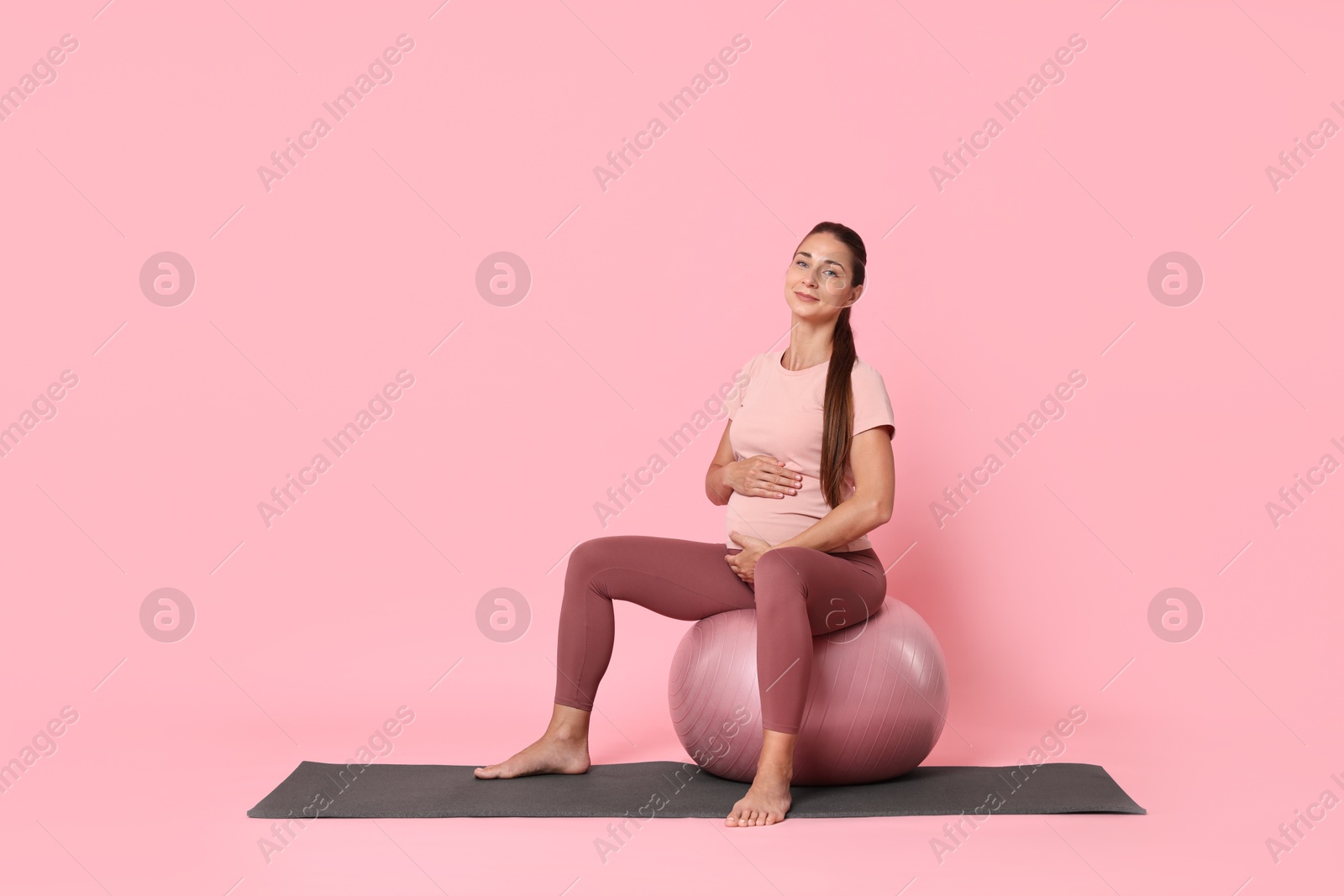 Photo of Beautiful pregnant woman doing exercises on fitball against pink background