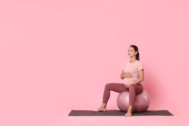 Photo of Beautiful pregnant woman doing exercises on fitball against pink background, space for text