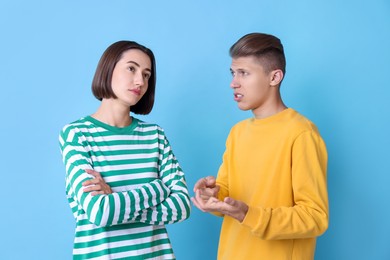 Emotional young couple having quarrel on light blue background