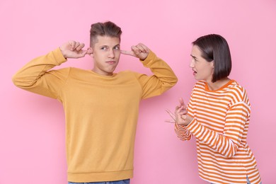 Emotional young couple arguing on pink background