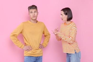 Emotional young couple arguing on pink background