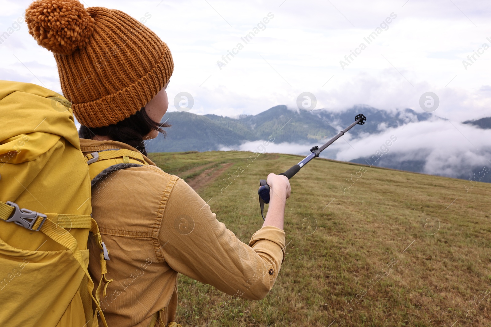 Photo of Young hiker with trekking poles and backpack in mountains outdoors, back view