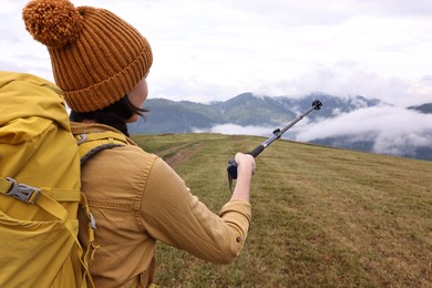 Young hiker with trekking poles and backpack in mountains outdoors, back view