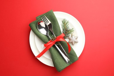 Photo of Beautiful Christmas setting with plates, elegant cutlery and festive decor on red table, top view