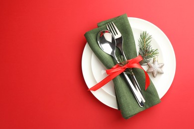 Photo of Beautiful Christmas setting with plates, elegant cutlery and festive decor on red table, top view. Space for text