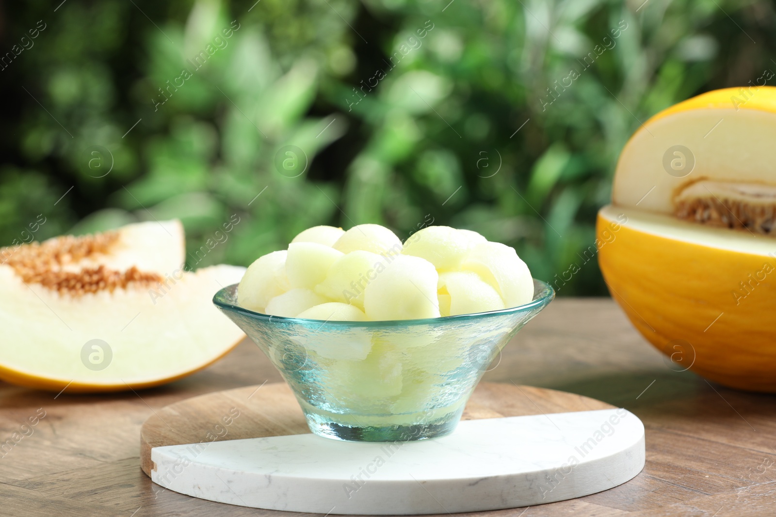 Photo of Fresh ripe melon balls in dessert bowl on wooden table outdoors