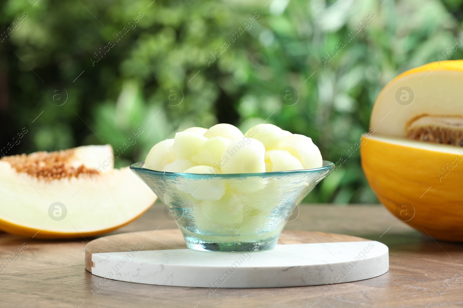 Photo of Fresh ripe melon balls in dessert bowl on wooden table outdoors