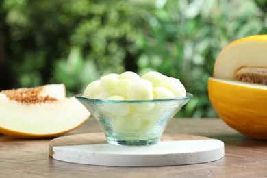 Fresh ripe melon balls in dessert bowl on wooden table outdoors