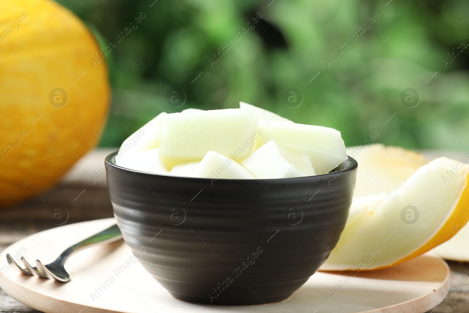 Photo of Cut fresh ripe melon in bowl served on table outdoors, closeup