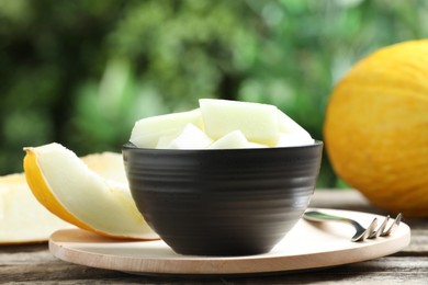 Photo of Cut ripe melon in bowl served on wooden table outdoors, closeup