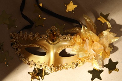 Beautiful golden carnival mask and confetti on beige background, closeup