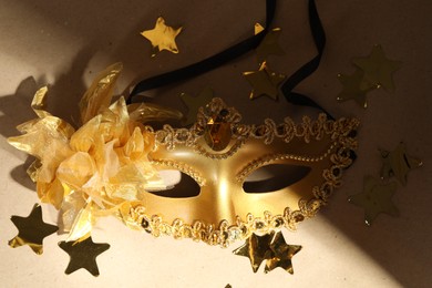 Beautiful golden carnival mask and confetti on beige background, closeup