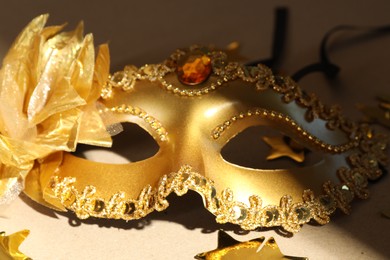 Photo of Beautiful golden carnival mask and confetti on beige background, closeup