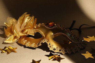 Beautiful golden carnival mask and confetti on beige background, closeup