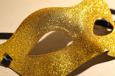 Photo of Beautiful golden carnival mask on beige background, closeup