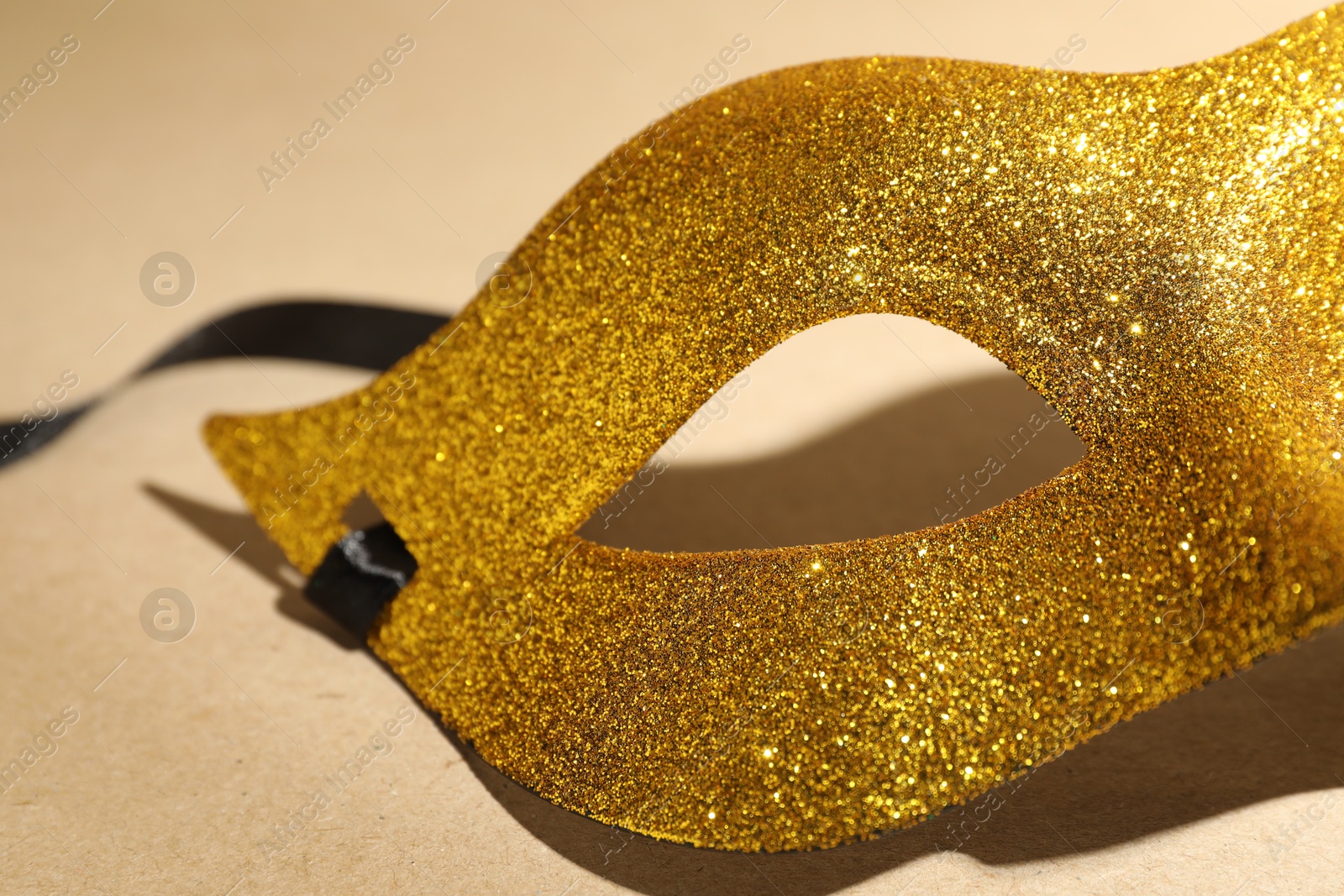 Photo of Beautiful golden carnival mask on beige background, closeup